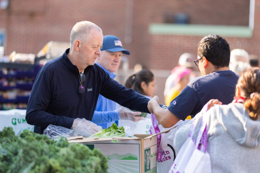 Male volunteer fills a customer's bag with food outside in a line of customers