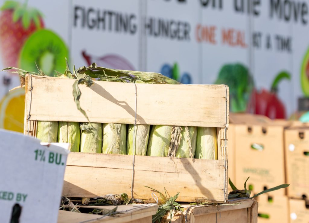 Crate containing ears of corn in front of a truck with the words "Fighting hunger one meal at a time" written on it