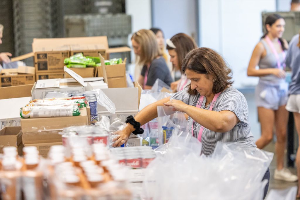 Woman packing meal bags in a warehouse with other female volunteers
